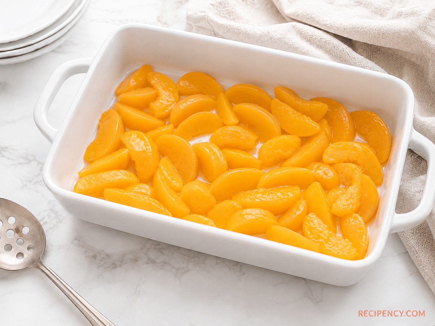 Sliced peaches spread evenly in a 9x13 baking pan for Peach Cobbler with Cake Mix