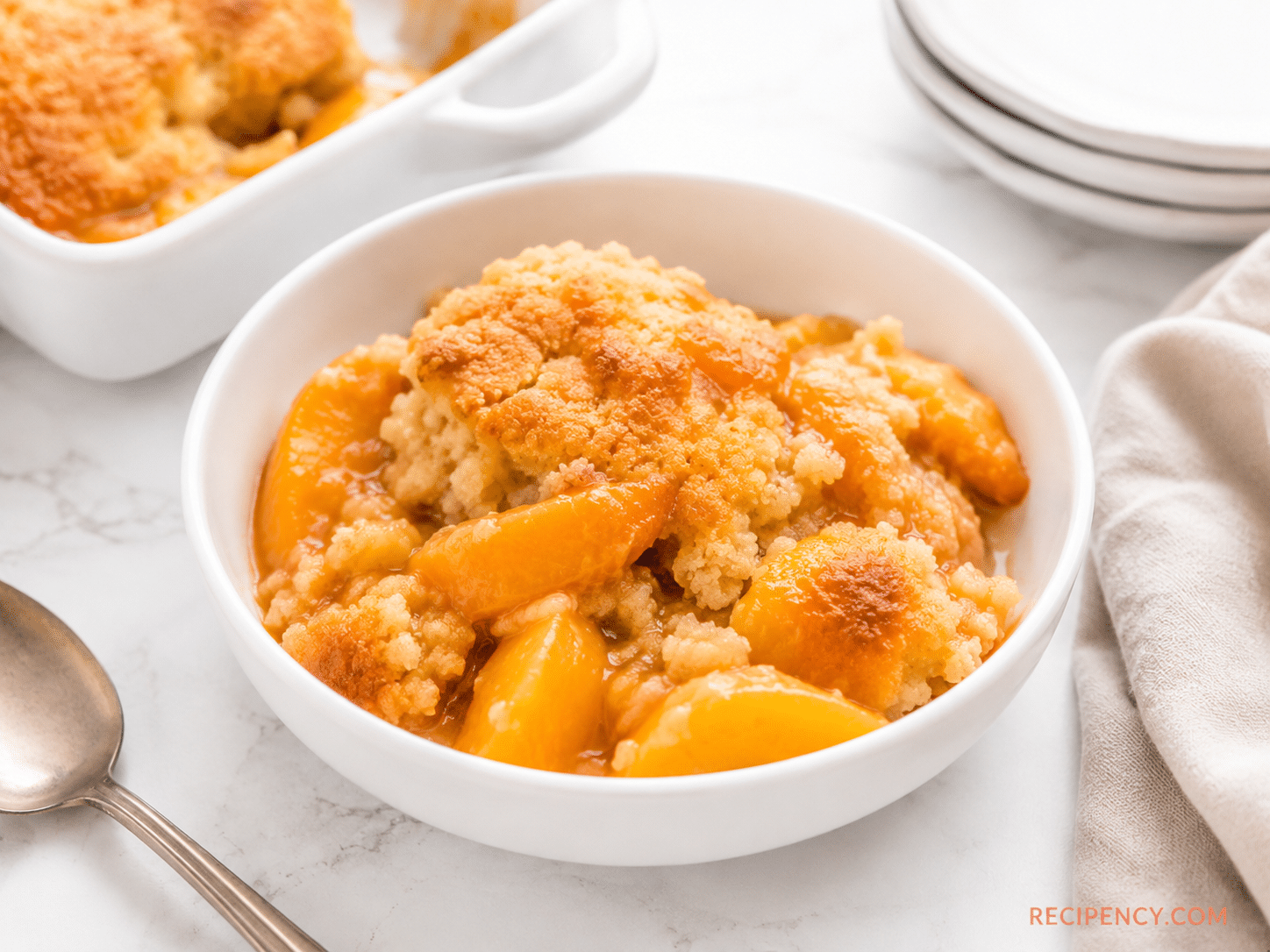 A warm scoop of Peach Cobbler with Cake Mix served in a white bowl