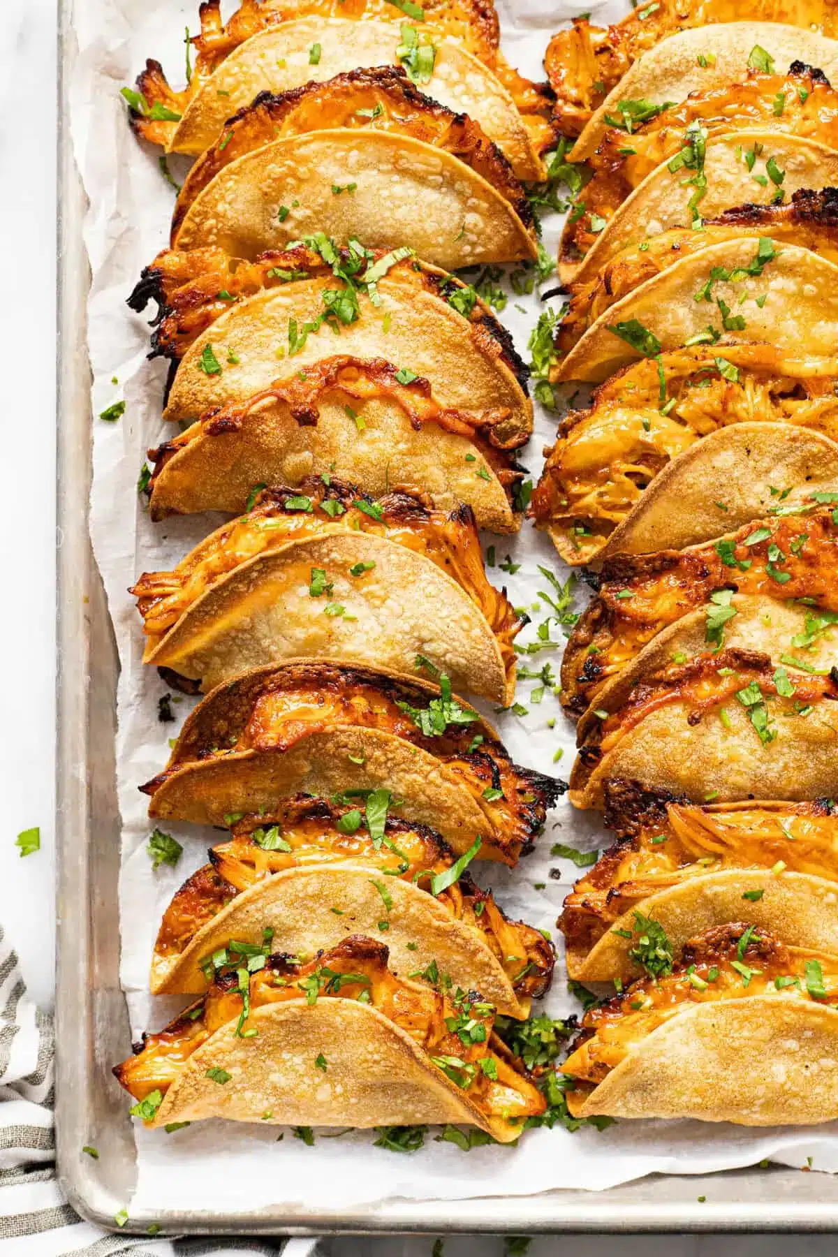 20-Minute Mini Tacos (Crispy Baked Chicken Tacos) 11 Overhead view of crispy baked Mini Tacos garnished with fresh cilantro on a parchment-lined baking sheet