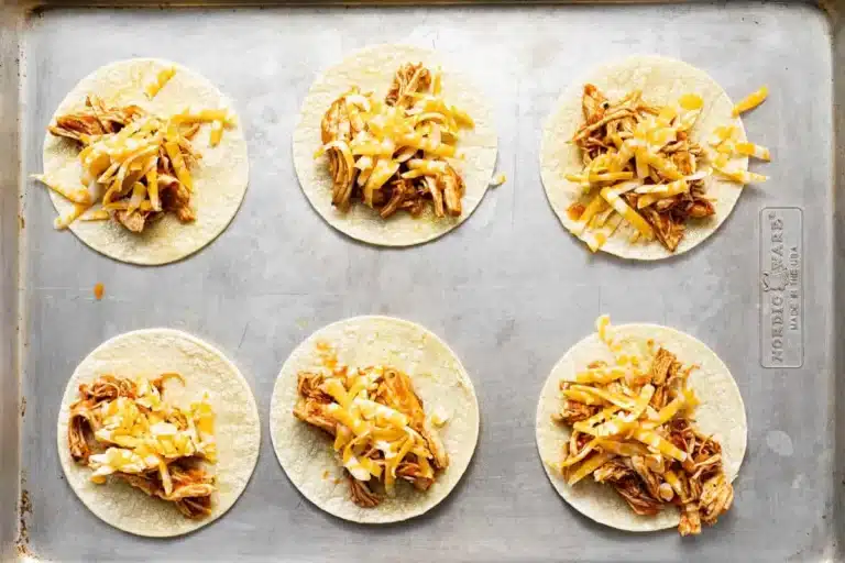 Unbaked Mini Tacos filled with seasoned chicken and shredded cheese on a metal baking sheet