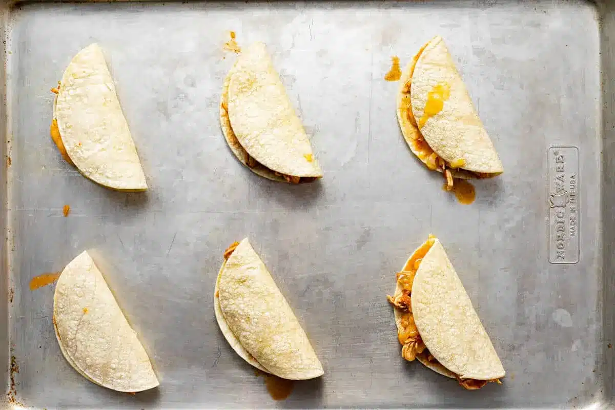 20-Minute Mini Tacos (Crispy Baked Chicken Tacos) 14 Folded Mini Tacos ready for the oven on a metal baking sheet
