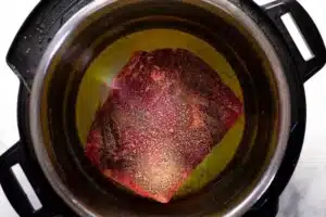 Raw chuck roast placed in the Instant Pot with heated olive oil