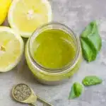 Healthy Lemon Basil Vinaigrette 11 Overhead view of a small glass jar filled with Lemon Basil Vinaigrette, surrounded by fresh basil leaves and lemon halves.