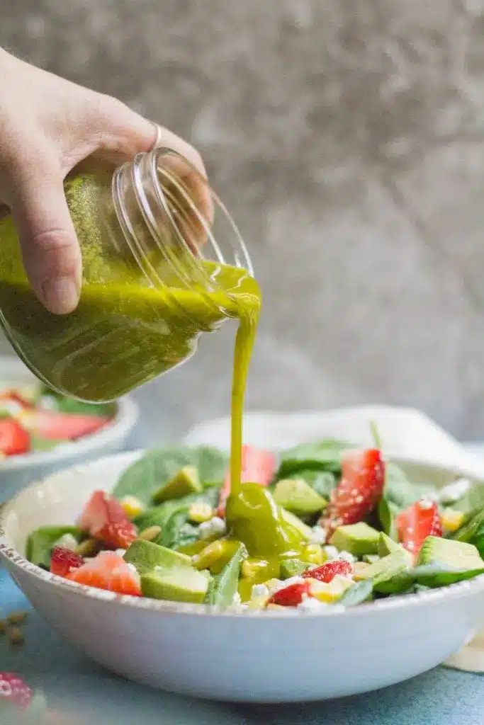 Healthy Lemon Basil Vinaigrette 9 Hand pouring homemade Lemon Basil Vinaigrette from a glass jar over a fresh green salad bowl.