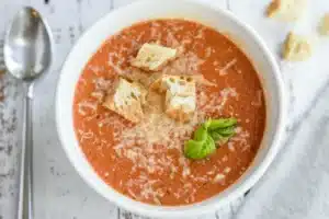 Close-up view of homemade Tomato Basil Soup with croutons and a spoon resting in the bowl.